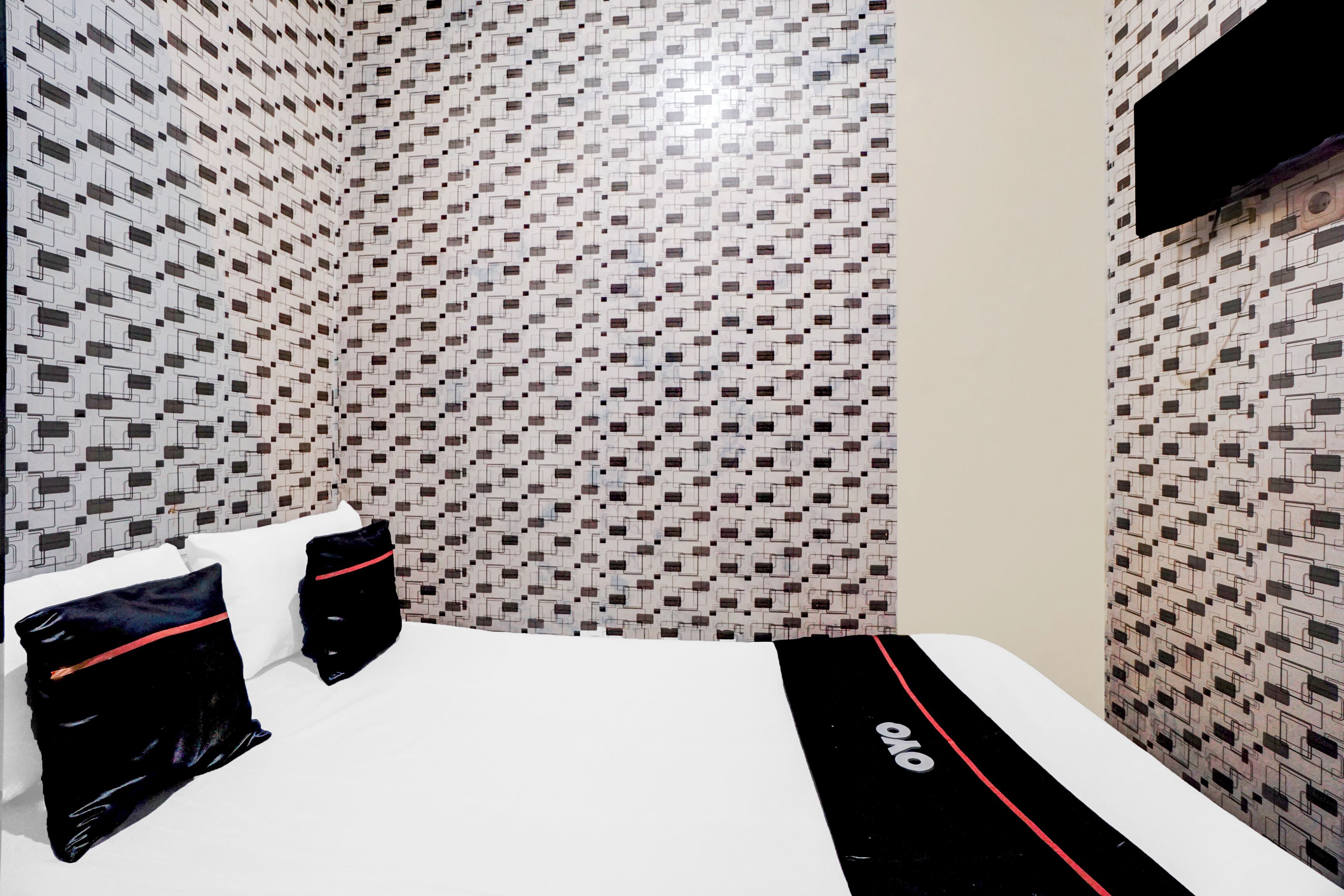 Habitación de hotel con pared estampada, cama con ropa blanca y almohadas negras, y colcha negra y roja.