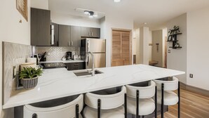 A modern kitchen with a central island, stainless steel appliances, and a herringbone tile backsplash.