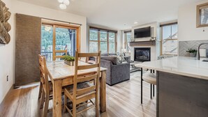 A modern kitchen with a large island, a dining area with wooden furniture, and a living room with a fireplace.