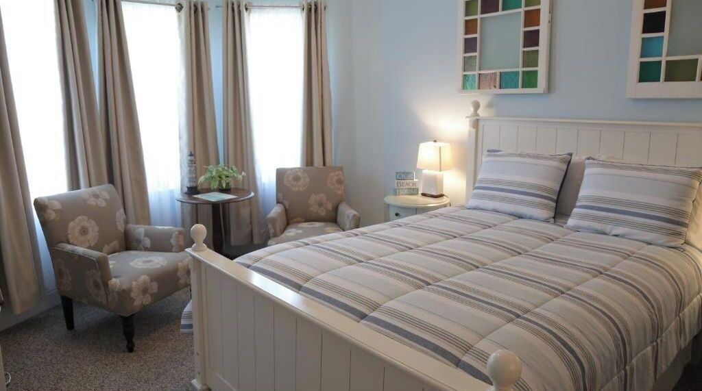 A bedroom with a bed, two chairs, a small table, and a lamp.