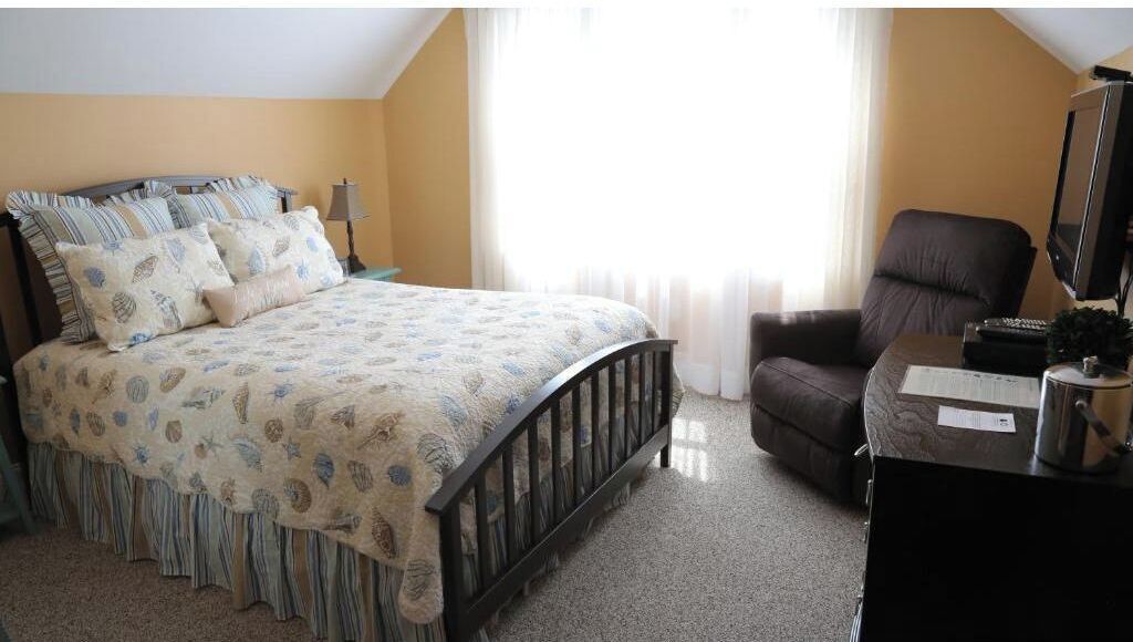Quarto com cama, cadeira, escrivaninha e televisão.