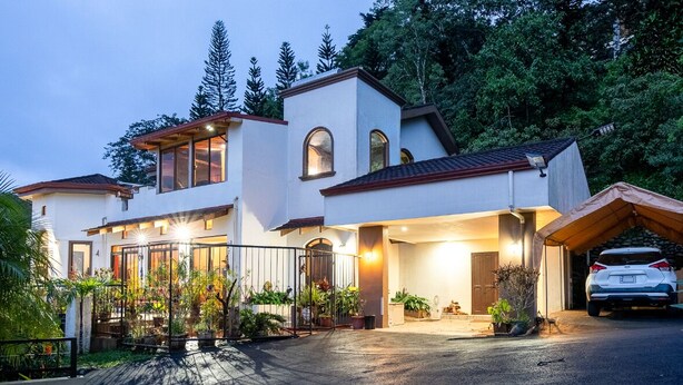 Una casa moderna de dos pisos con garaje, rodeada de abundante vegetación.