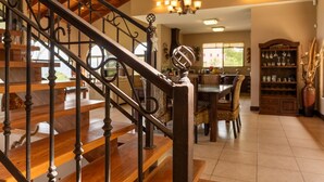 Un comedor amplio con escaleras de madera, muebles de mimbre y una estantería para vinos.