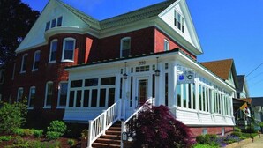 A two-story brick building with a white front porch and a staircase leading to the entrance. - Savannah Inn Bay Breeze (Lewes)