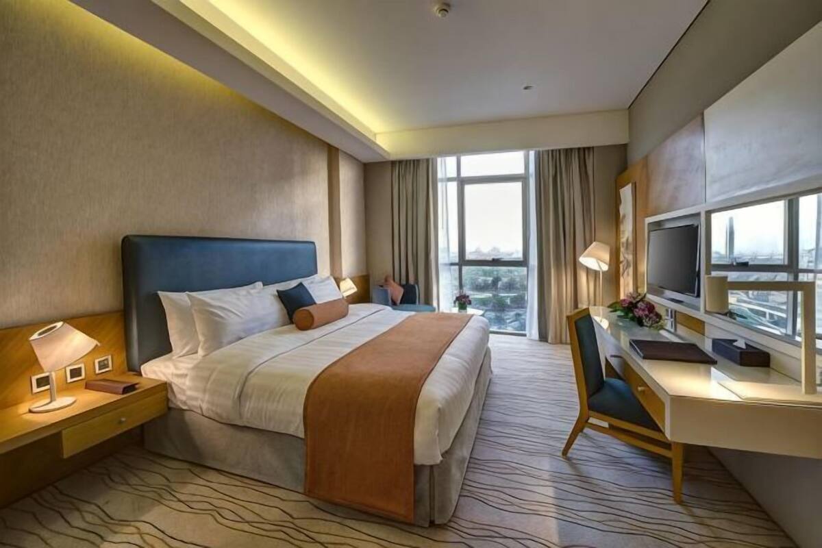 A hotel room with a large bed, a desk, a TV, and a view of the city.