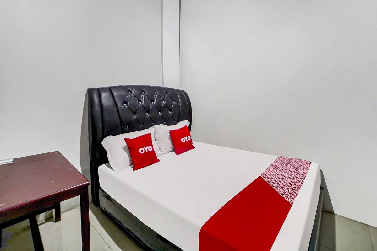 A bed with a tufted headboard, white bedding, and red pillows with "OYO" branding.