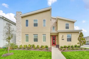 A two-story building with a beige facade, a red door, and a stone chimney. - Storey Lake 9 BR Themed Games Room (Kissimmee)