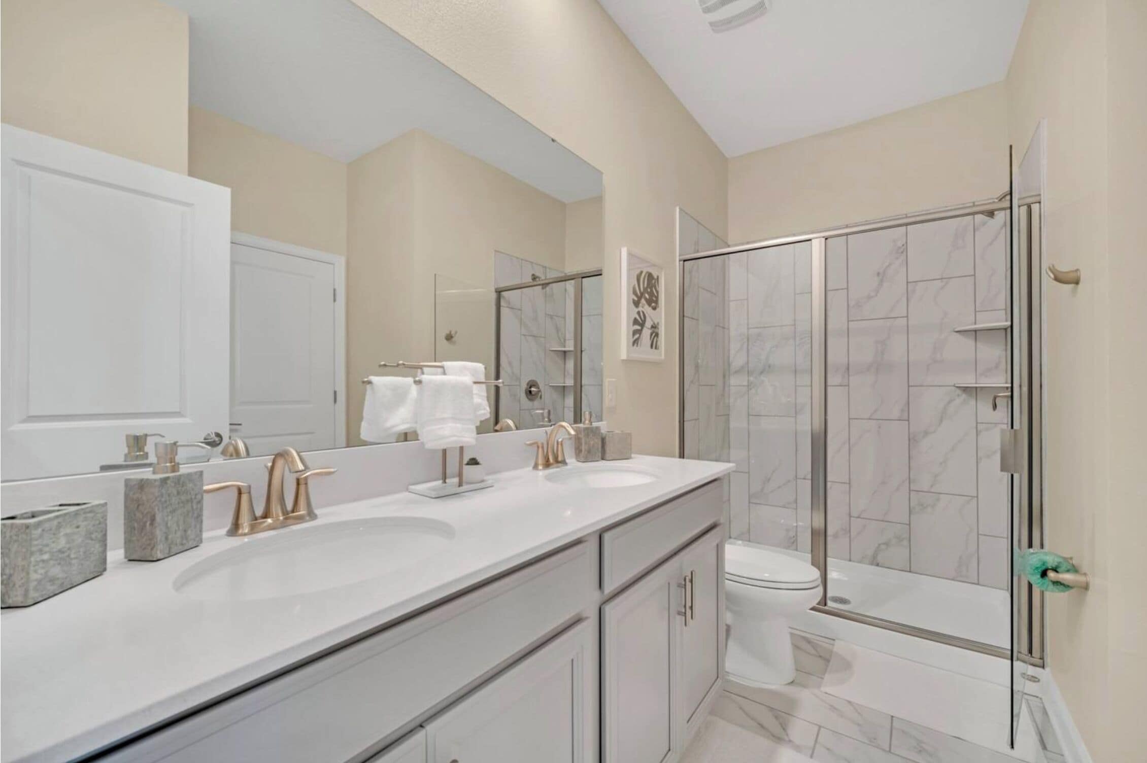 Une salle de bain moderne avec un grand miroir, deux lavabos, une douche et des toilettes.