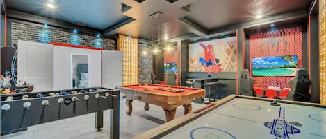 A modern indoor recreational area with a foosball table, pool table, and a large TV screen.