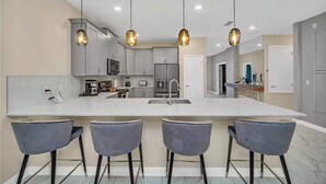 A modern kitchen with a large island, bar stools, pendant lighting, and stainless steel appliances. - Storey Lake 9 BR Themed Games Room (Kissimmee)