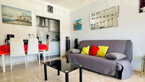Un salon moderne avec un canapé gris, des coussins rouges et jaunes, une table basse noire et un coin repas blanc avec des chaises rouges.