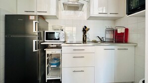 Une cuisine moderne avec des meubles blancs, un réfrigérateur noir, un four à micro-ondes et un évier en acier inoxydable.
