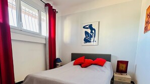 Une chambre à coucher avec un lit, des rideaux rouges, une table de chevet, une lampe et une œuvre d’art murale.