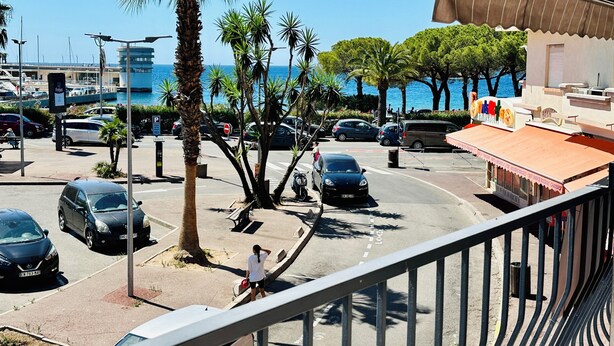 Une rue côtière bordée de voitures garées, de palmiers et d’un immeuble doté d’un auvent rouge.