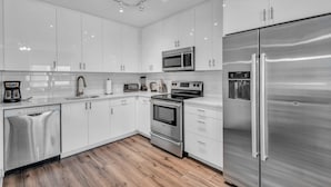 A modern kitchen with white cabinets, stainless steel appliances, and a wooden floor. - Luxury 4BD Condo Near French Quarter – Prime Location! (New Orleans)