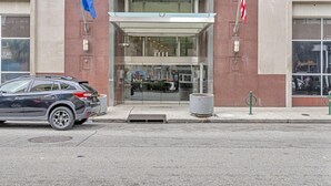 A modern building with a glass entrance, a flag, and an American flag. - Luxury 4BD Condo Near French Quarter – Prime Location! (New Orleans)