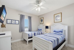 Un dormitorio con dos camas, ventilador de techo, televisor y ventana con cortinas.