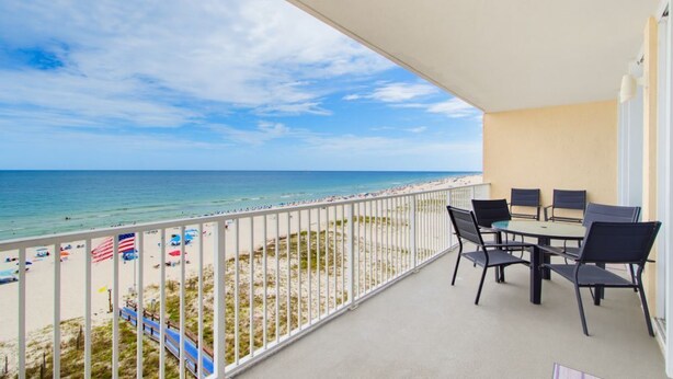 Ein Balkon mit Blick auf den Strand, einem Tisch mit Stühlen und einer Geländer.