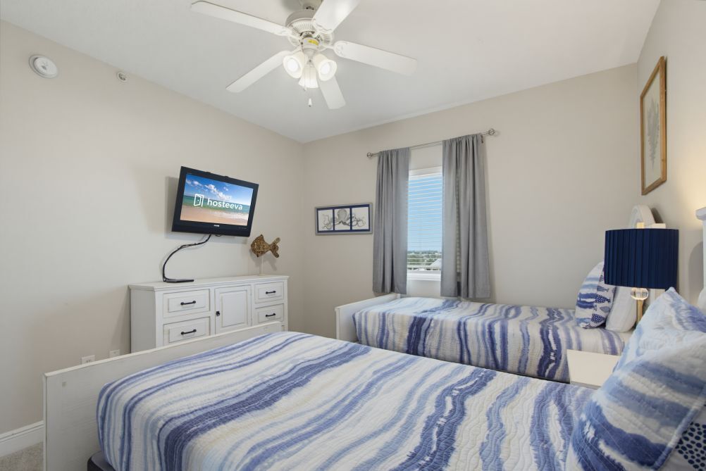 A bedroom with two beds, a ceiling fan, a TV, a dresser, and a window with curtains.