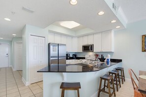 Una cocina moderna con armarios blancos, una encimera negra y un refrigerador de acero inoxidable.