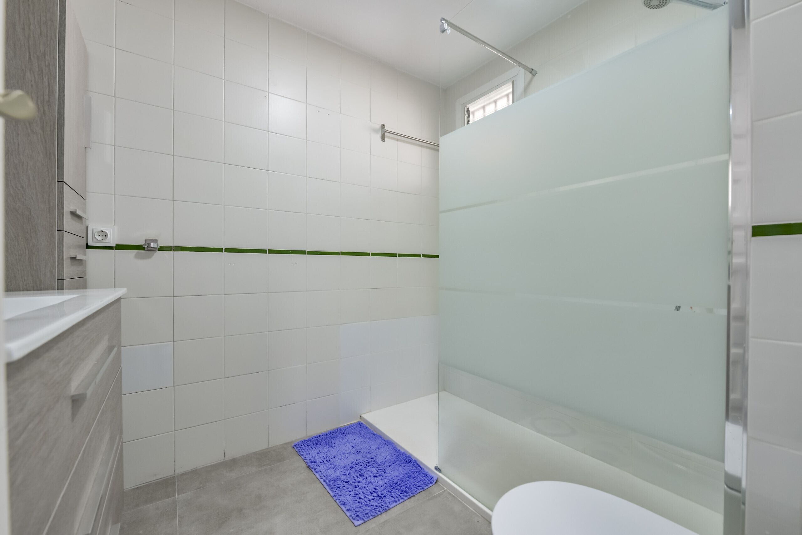 Une salle de bain moderne avec des carreaux blancs, une douche en verre, un tapis de bain bleu et une bande verte sur le sol.