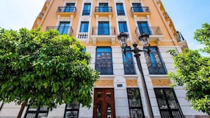A multi-story building with balconies, a central entrance, and surrounding greenery.