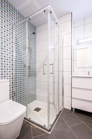 A modern bathroom with a glass-enclosed shower, white tiles, and a patterned wall.