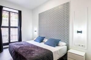 A bedroom with a bed, a patterned headboard, a window with curtains, and a door with a light switch.