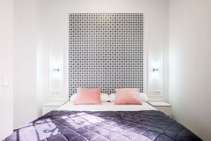 A bedroom with a patterned wallpaper, a bed with two pillows, and bedside lamps.