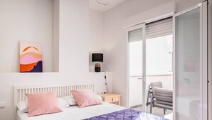 A bedroom with a bed, a nightstand, a lamp, a painting, and a sliding glass door to a balcony. - Beautiful Suite with Private Terrace (Valencia)