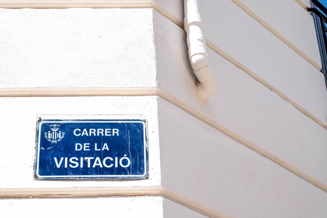 A blue sign with white lettering on a building wall, reading "CARRER DE LA VISITACIÓ".