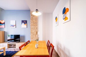 A modern living room with a wooden dining table, red chairs, a TV, and abstract art on the walls.
