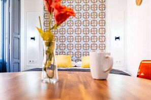 A hotel room with a patterned wall, a wooden table, a white mug, a vase with flowers, and a red chair. - Classy Studio Apartment with Unique Design (Valencia)