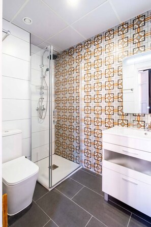 A modern bathroom with a glass shower enclosure, a white toilet, and a vanity with a mirror. - Classy Studio Apartment with Unique Design (Valencia)