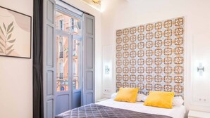 A bedroom with a bed, two yellow pillows, a patterned wall, and a window with a view of buildings. - Classy Studio Apartment with Unique Design (Valencia)