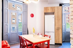 A compact kitchen with a wooden table and chairs, a white refrigerator, and a red clock on the wall.