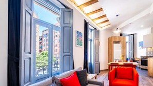 Uma sala de estar moderna com um sofá cinzento, cadeiras vermelhas e janelas grandes com vista para edifícios.