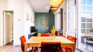 Uma sala de estar moderna com uma mesa de jantar, cadeiras, uma TV e uma grande janela com vista para a cidade.