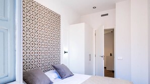 A bedroom with a patterned headboard, a bed with white bedding, two pillows, and a door leading to another room.