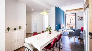 A modern kitchen with white cabinets, a white dining table with red chairs, and a hanging pendant light.