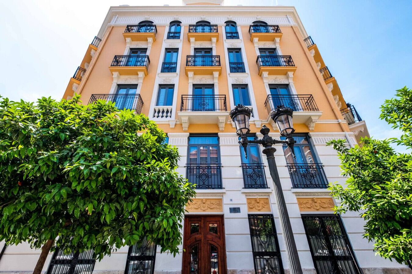 A multi-story building with balconies, a central entrance, and a street lamp.