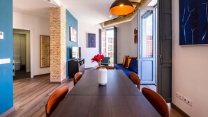 A modern living room with a long wooden table, a brick accent wall, and a large window. - Well Lit and Creatively Designed Apartment (Valencia)