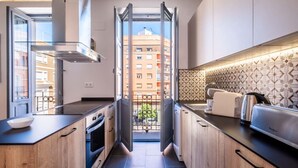 A modern kitchen with wooden cabinets, a stainless steel range hood, and a view of a balcony with buildings in the background. - Well Lit and Creatively Designed Apartment (Valencia)