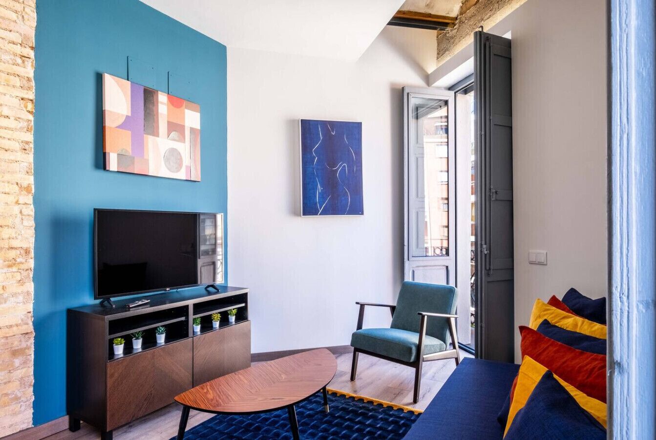 Een moderne woonkamer met een flatscreen televisie, een houten salontafel, een blauwe bank en een blauwe fauteuil.