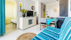Een moderne woonkamer met een bank, een televisie, een eethoek met een tafel en stoelen, en een keuken met een koelkast en een televisie.