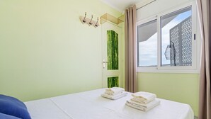 Een hotelkamer met een bed, een raam met gordijnen, een deur met een groene decoratieve panelen en een wandlamp.