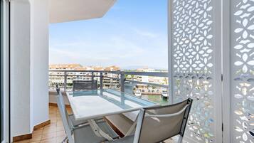 A balcony with a glass table and chairs, overlooking a marina and buildings.