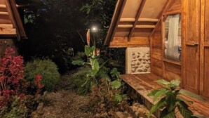 Een houten hutje met een schuin dak, een pad van stenen en omliggende beplanting.