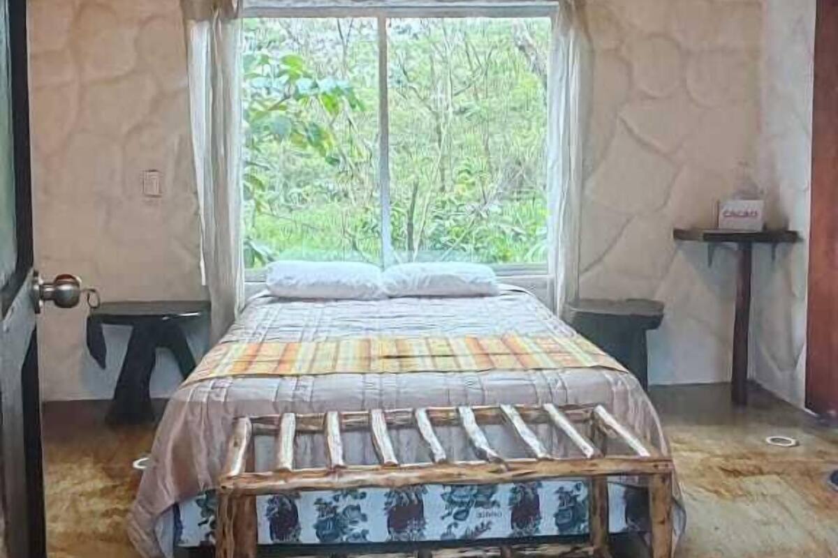 Une chambre à coucher au style rustique, avec un mur en pierre, un cadre de lit en bois et une fenêtre donnant sur un paysage verdoyant.