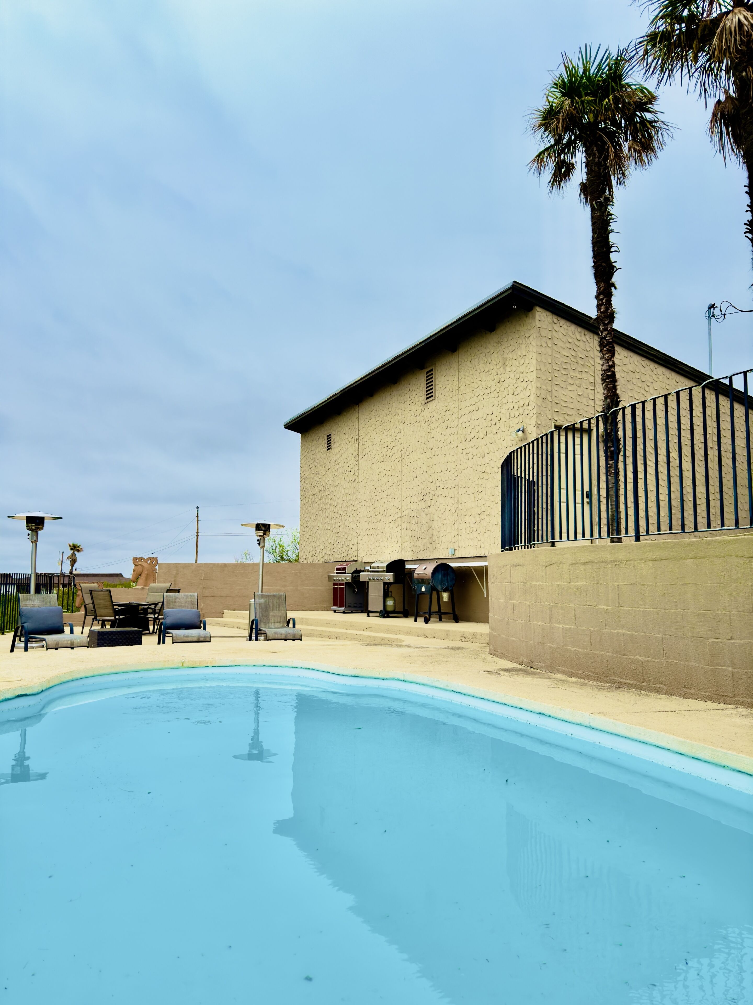 A swimming pool with lounge chairs, a barbecue area, and a building with a textured facade.